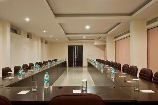 A long conference room set up in a U-shape, with chairs, water bottles, and glasses on the tables, under bright overhead lights.