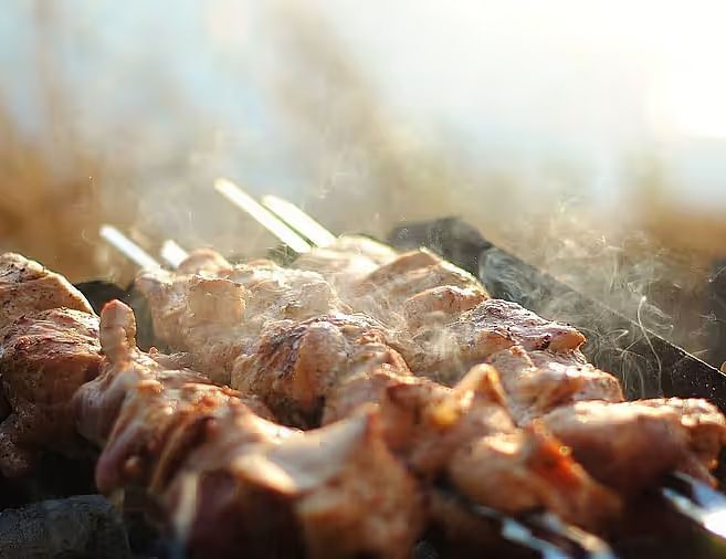 Juicy skewered meat being grilled over an open flame with smoke rising.