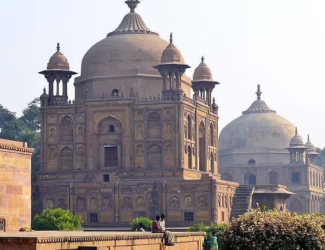 A grand historical structure with domes, set in a serene landscape - Khusro Bagh.
