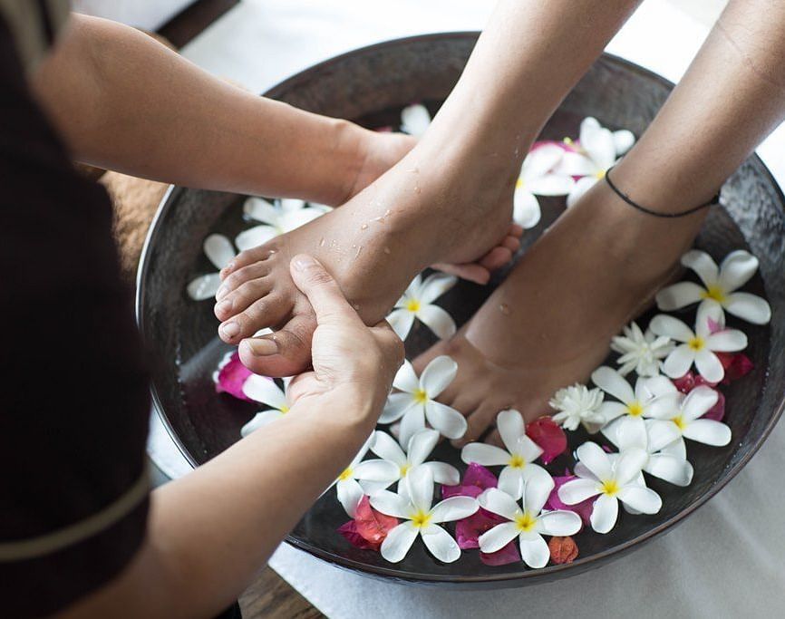 An image of foot soaked in water with fragrant flowers.
