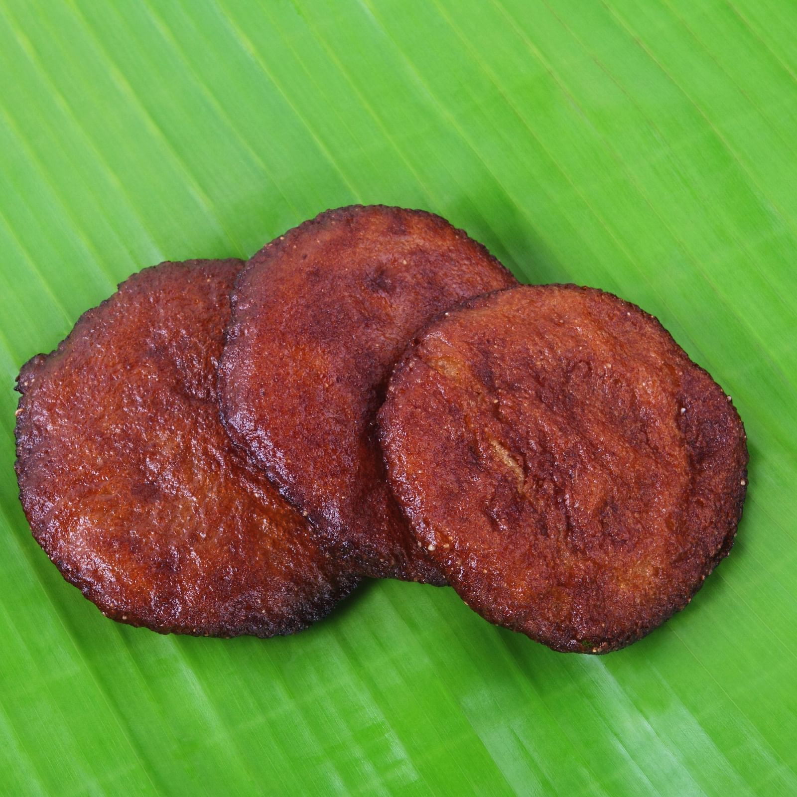 Three round, deep-fried plantain fritters neatly arranged on a vibrant green banana leaf.
