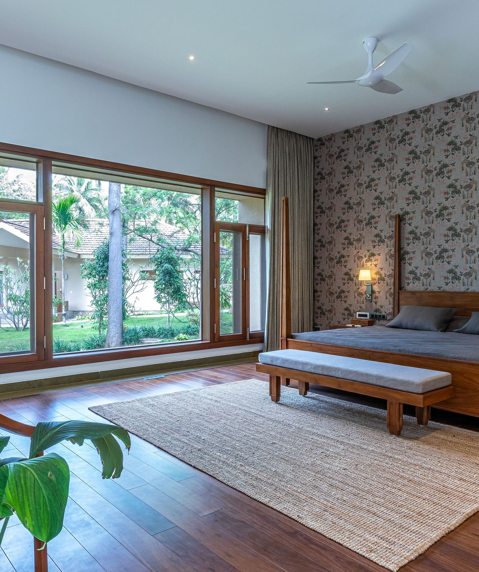 Bedroom with wooden furniture, large windows, rug, indoor plants, natural light - Shreyas Retreat