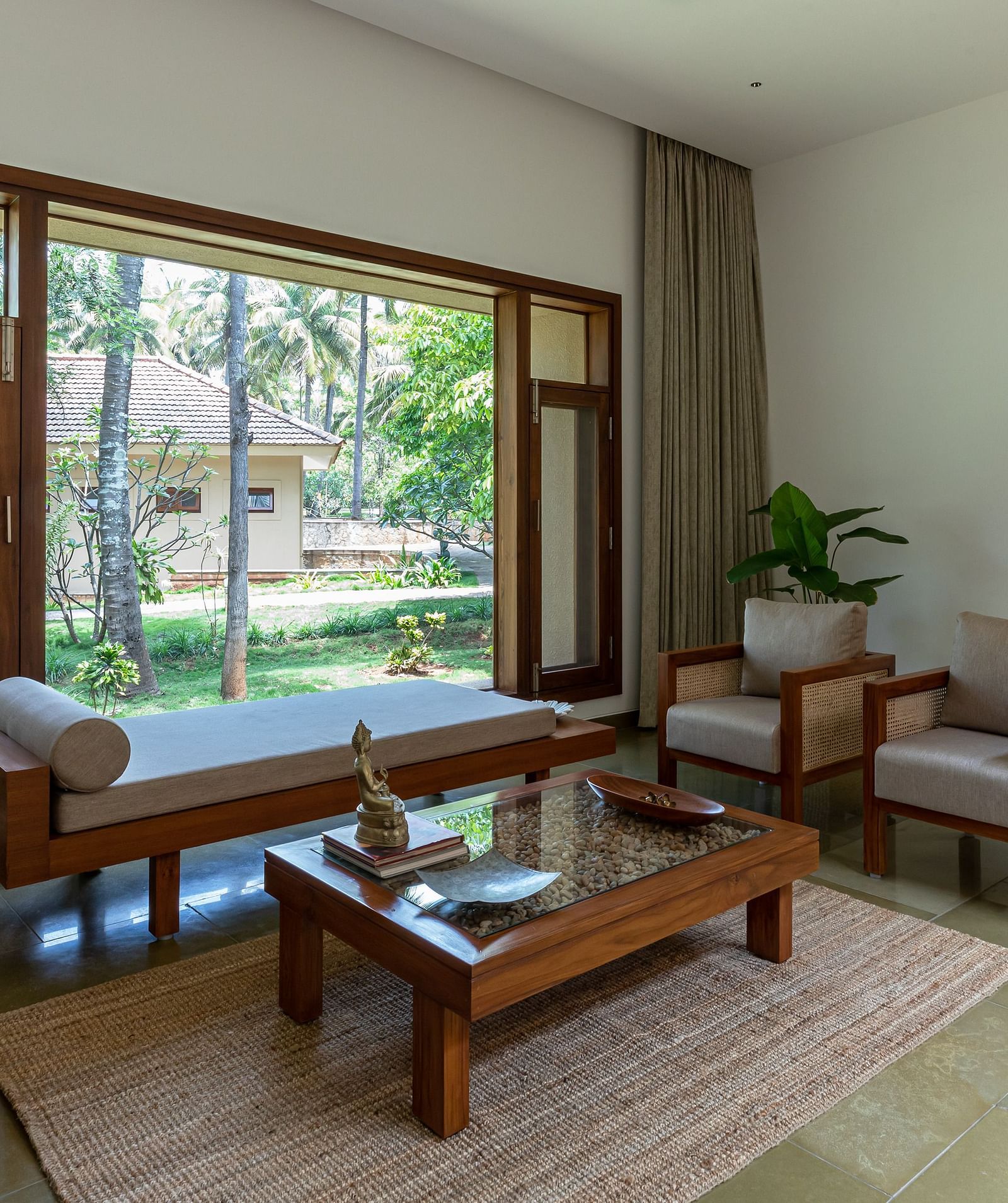 Living room with wooden furniture, rug, and large windows overlooking a garden, spacious interior - Shreyas Retreat