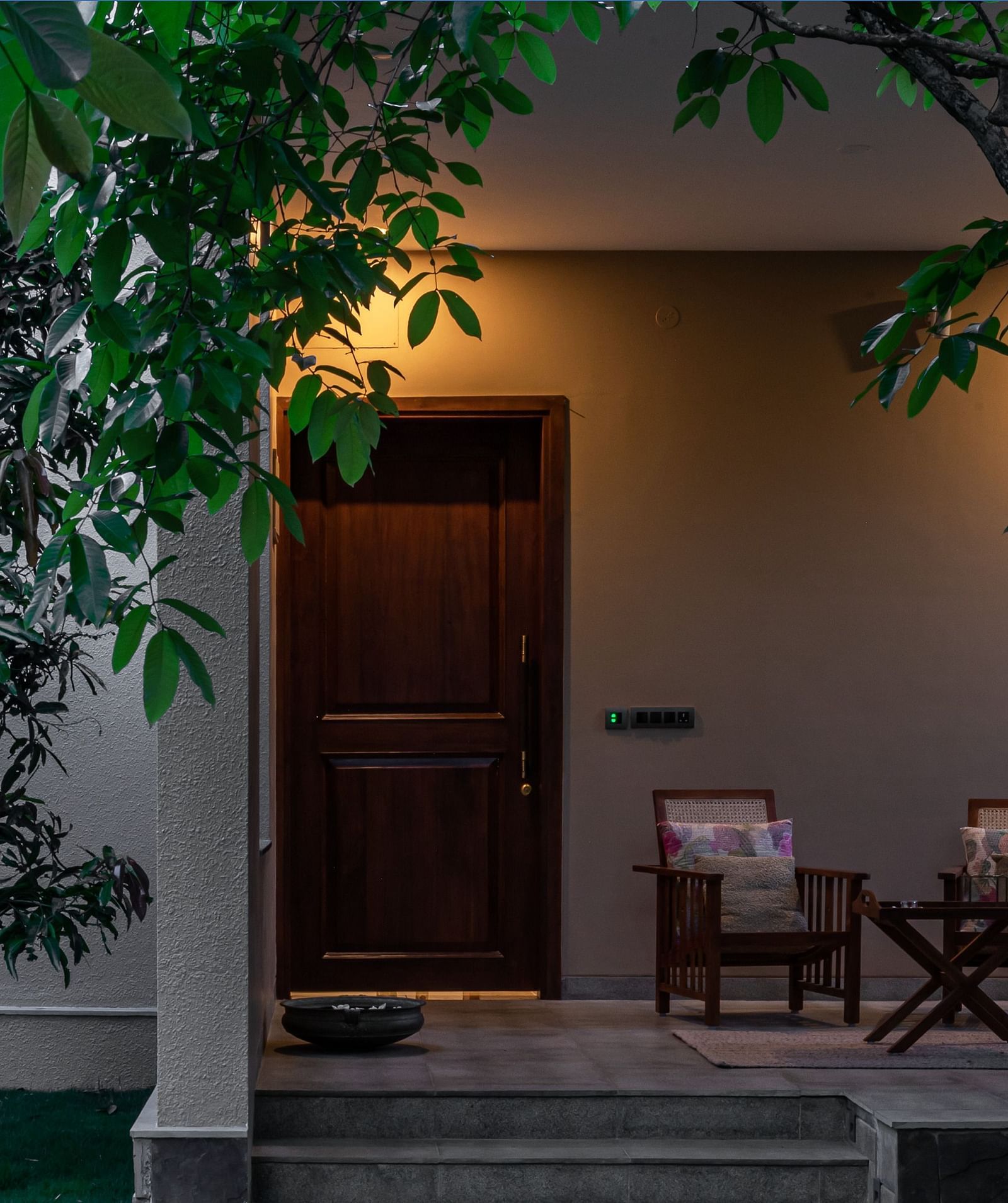 Exterior of a building with a door, chairs, and trees, outdoor lighting, stone pathway - Shreyas Retreat