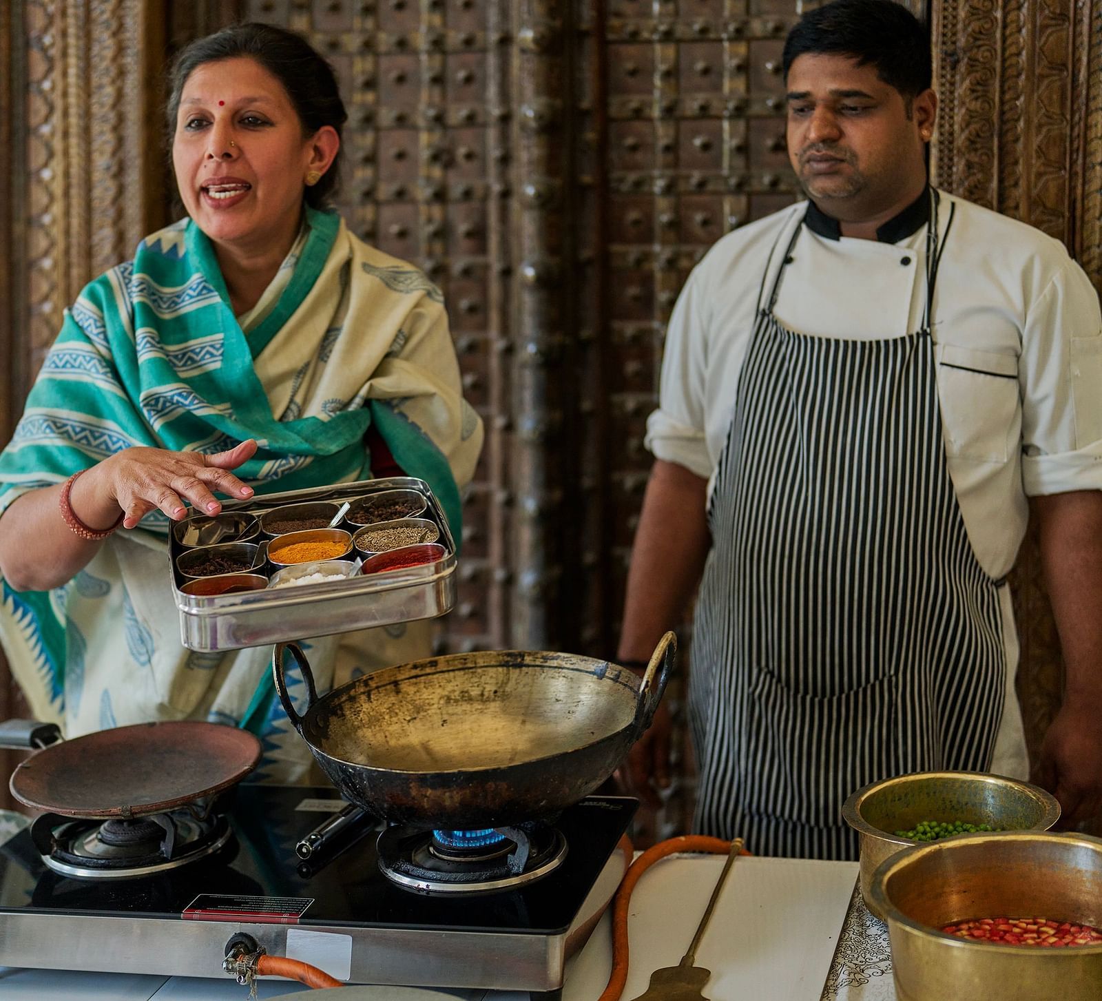 image of a woman explaining the spices in the box with another chef in the back supervising the process at dev shree, deogarh