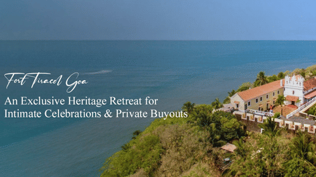 Scenic coastal view of Fort Tiracol Goa heritage retreat with red-tiled roofs and white walls on cliffside overlooking ocean, with text promoting intimate celebrations and private buyouts.