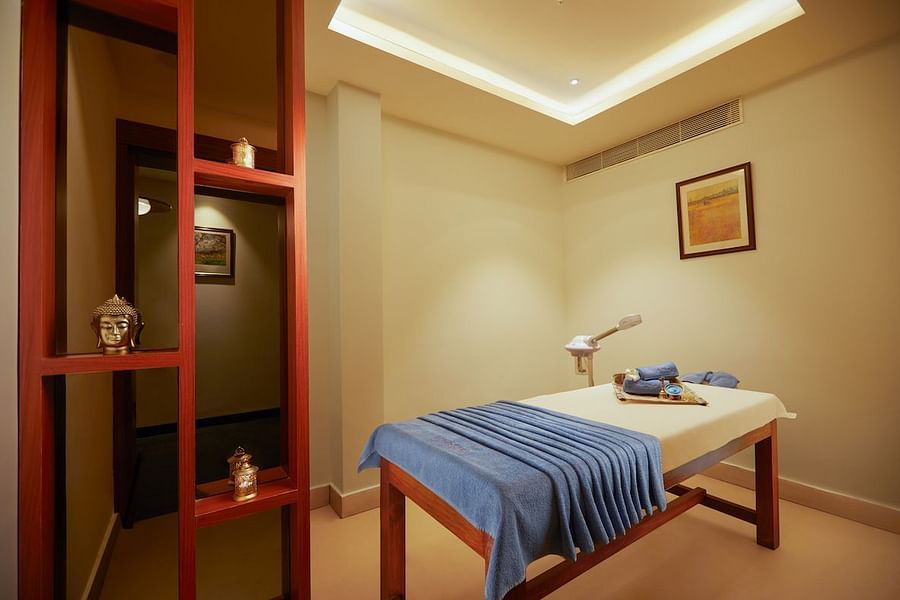 A massage table with a folded cloth in a room with a red-framed partition and a small picture on the wall.