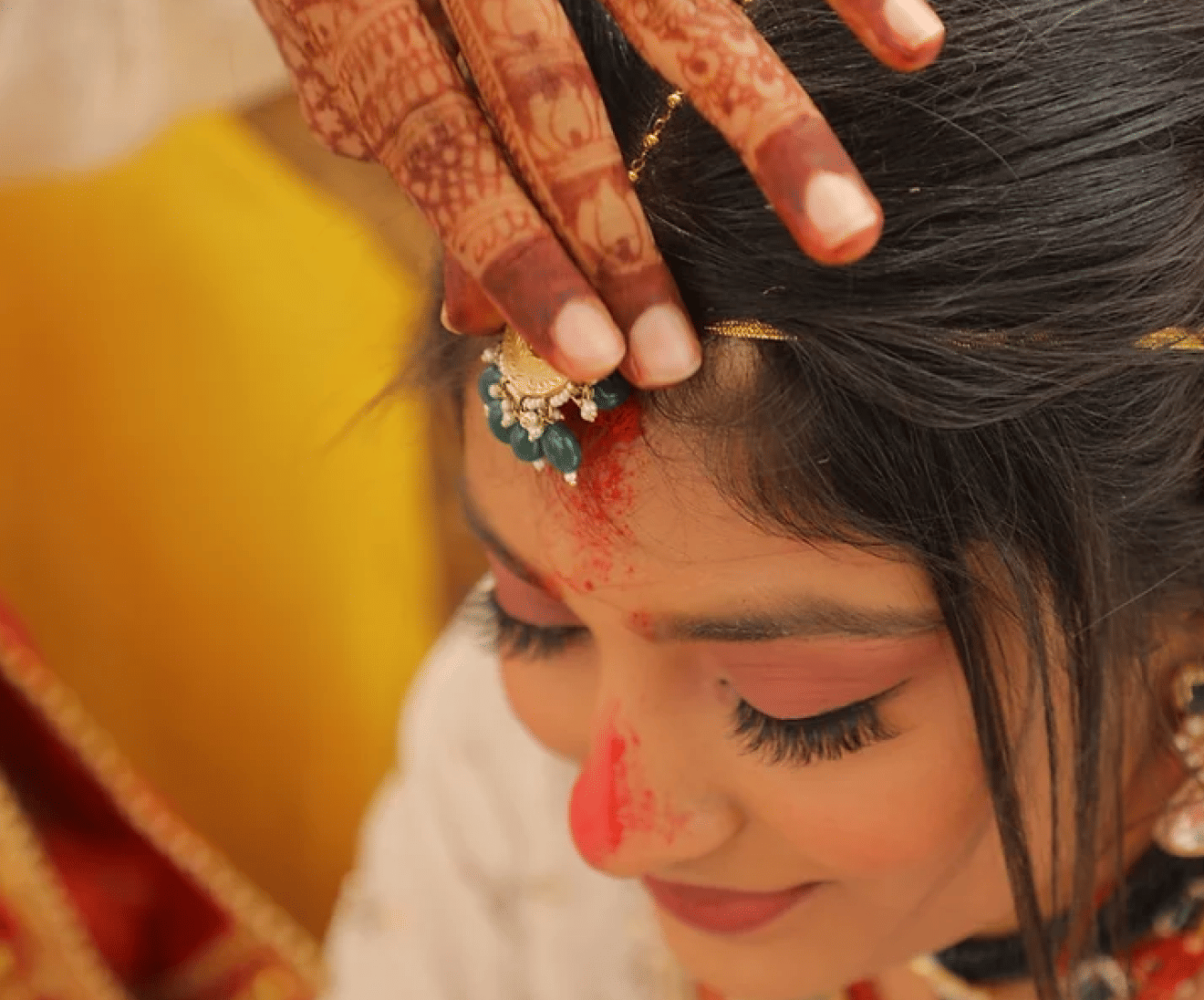 Image of a woman having her maang tikka adjusted.