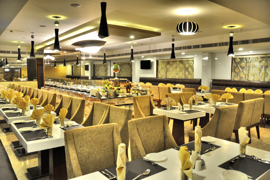 A spacious and elegantly lit restaurant with plush seating, neatly set tables, and a buffet counter – Raj Park Hotel in Alwarpet, Chennai