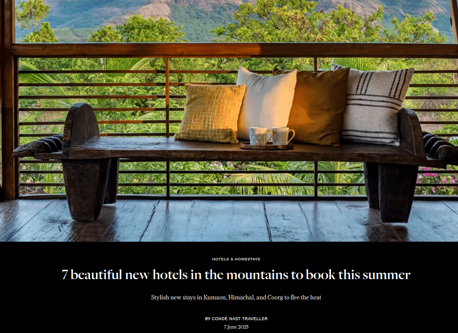 News article titled 7 beautiful new hotels in the mountains to book this summer, with an image showing a rustic wooden bench with four cushions and two mugs on a tray, placed on a wooden floor overlooking lush greenery and distant mountains.