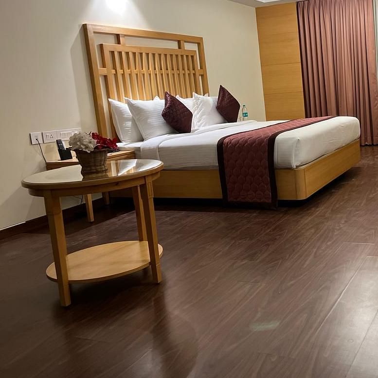 A corner view of the modern, well-lit bedroom with a king-size bed, a flat-screen TV, and a desk at MM legacy, Kanchipuram