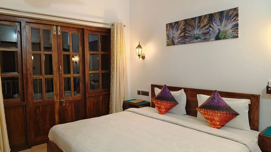 A double bed with colourful pillows and a frame hanging on the wall at 103 room at Ananda Holiday Home, Wayanad 4