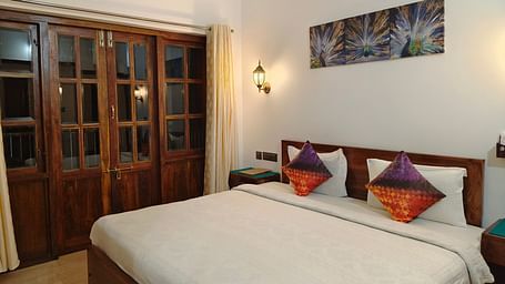 A double bed with colourful pillows and a frame hanging on the wall at 103 room at Ananda Holiday Home, Wayanad 4