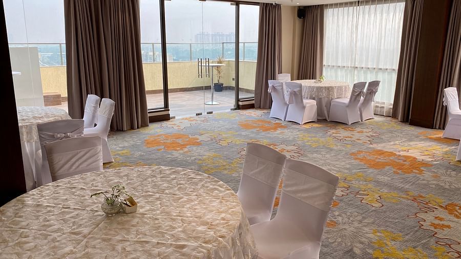 An image of a banquet hall with its seating arrangement, subtle decoration with lighting and an expansive glass door leading outdoor - Hideaway banquets & Lawns, Greater Noida