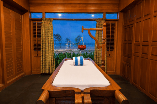Spa massage room with warm wooden interiors and soft evening lighting at Chariot Beach Resort, offering a calm and relaxing ambiance.