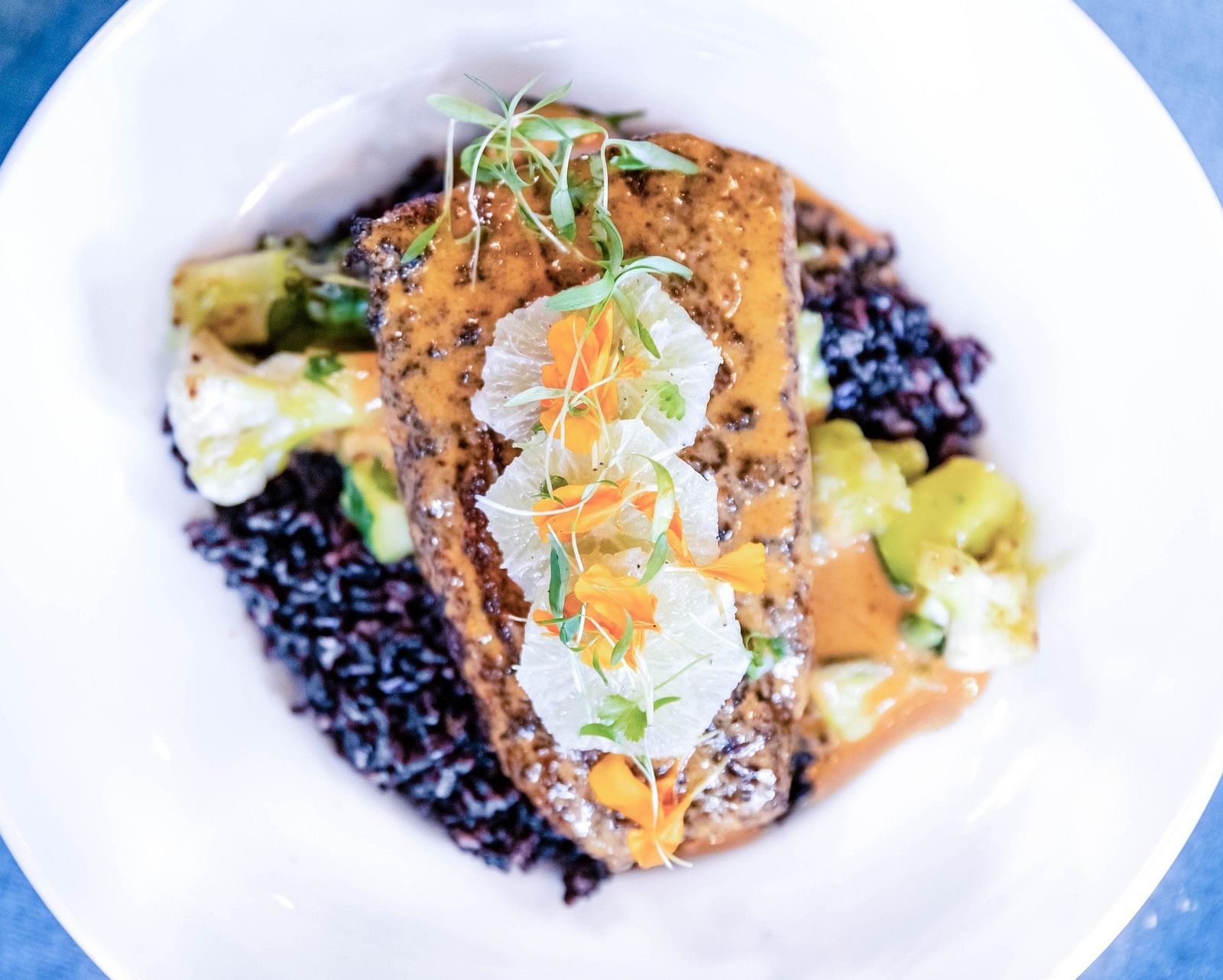 Top view of a well made dish with eggs on top and a layer of crisp followed by black edibles as base on a white plate 