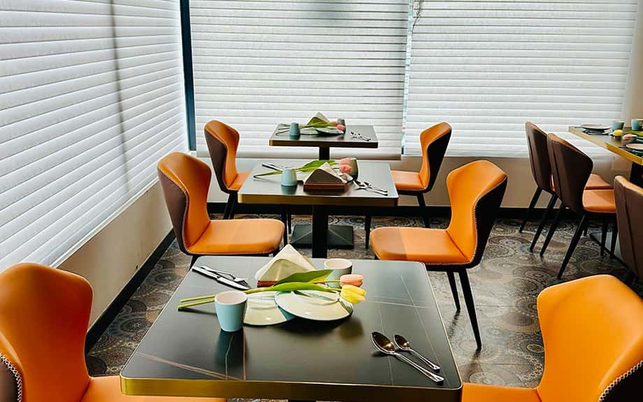 Dining hall with orange and brown chairs, a wall-mounted television, and a hanging fern