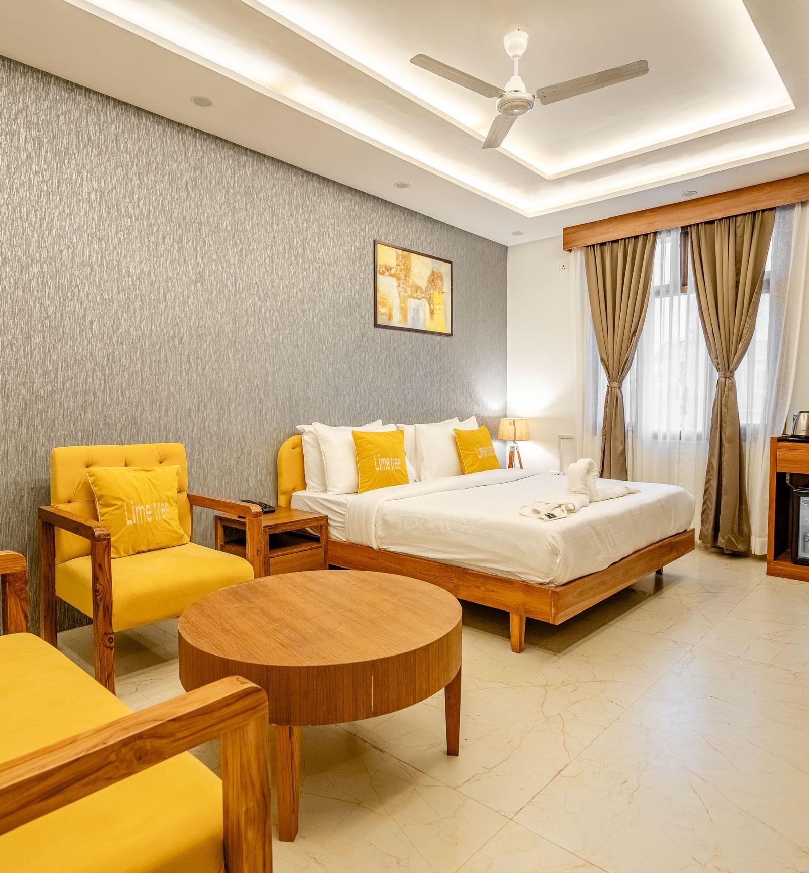 A bedroom with a king bed, cushions, pillows, bed sheets, coffee table, sofa chairs, wall decor, and designer ceiling lights at Lime Tree Hotels & Service Apartment Pvt Ltd.