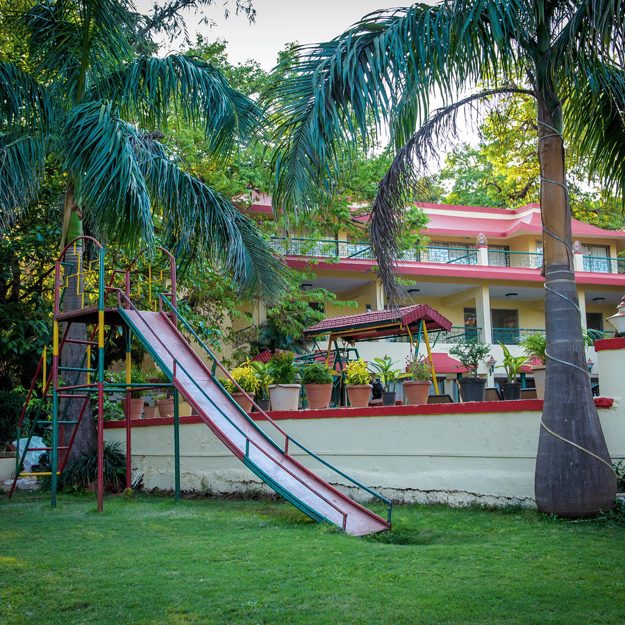 A play area for kids with a slide and surrounded by palm trees and the buildings.