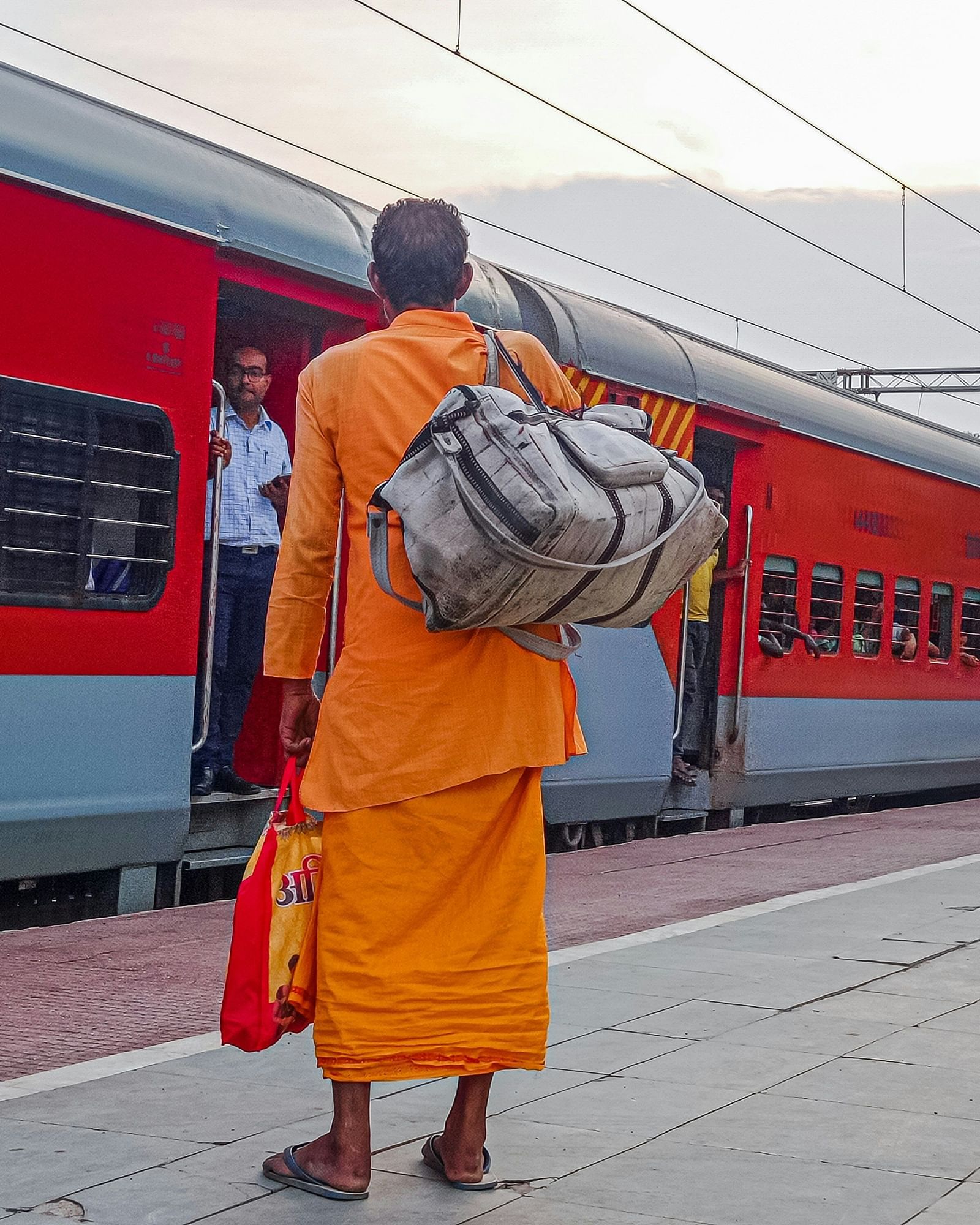 A person with bags stands on a train platform next to a parked train with open doors.