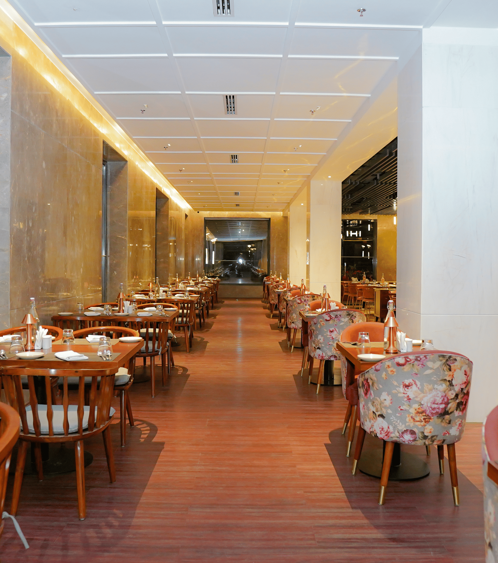 A long, well-lit indoor dining corridor with wooden and floral upholstered seating at Pushkara Resort & Spa.