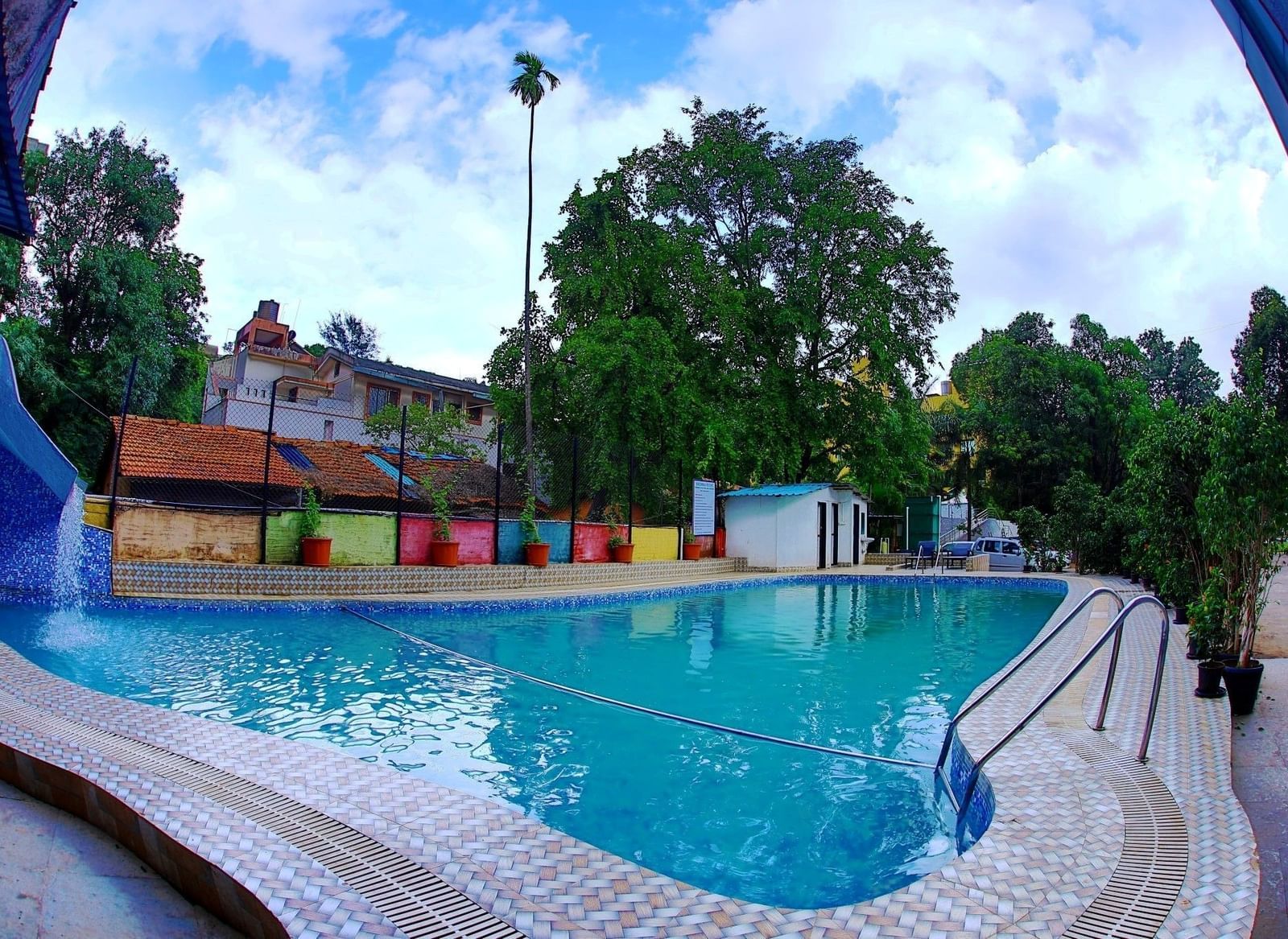 Assymetrical large swimming pool at Krushnai Resort under a partly cloudy blue sky.