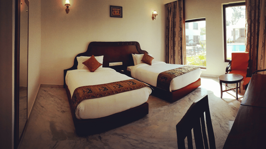 A twin-bedded room with chairs and a window view at AS Hotels, Khajuraho.