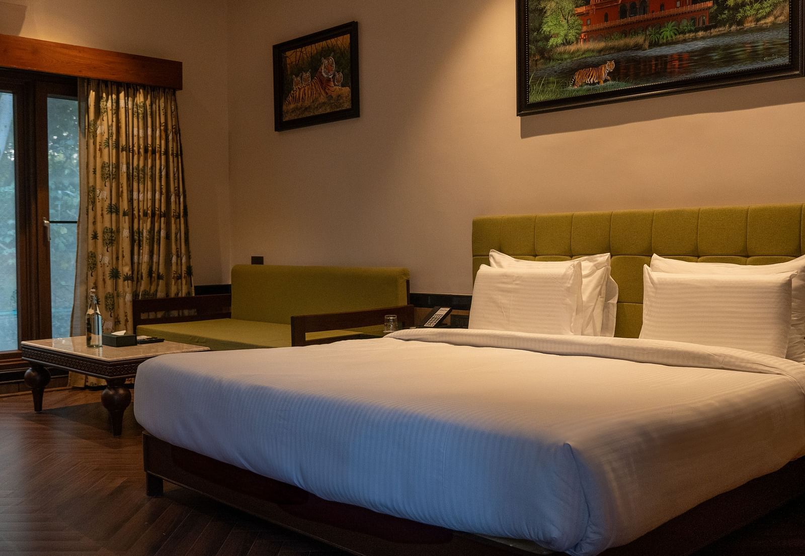 A well-appointed room at Aamaghati Jungle Retreat, Ranthambore, showcasing a bed with crisp white linens, a comfortable sofa, and framed artwork.