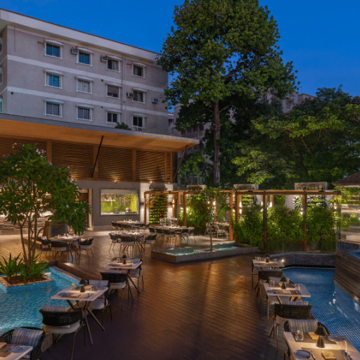 An outdoor swimming pool with a bar and lounge area, surrounded by lush greenery.