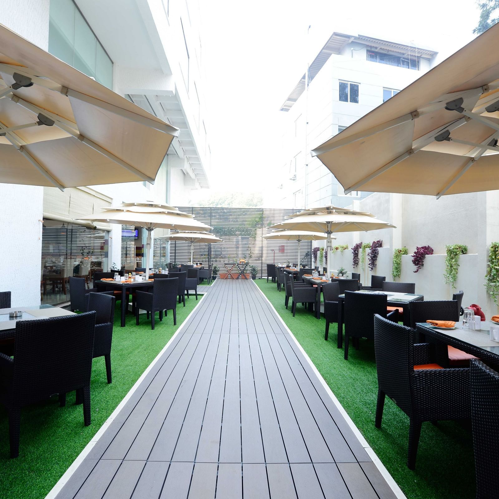Coffee Shop at The Cunningham Hotel featuring outdoor dining space with black wicker furniture, green flooring, large umbrellas, and elegant table settings featuring orange napkins
