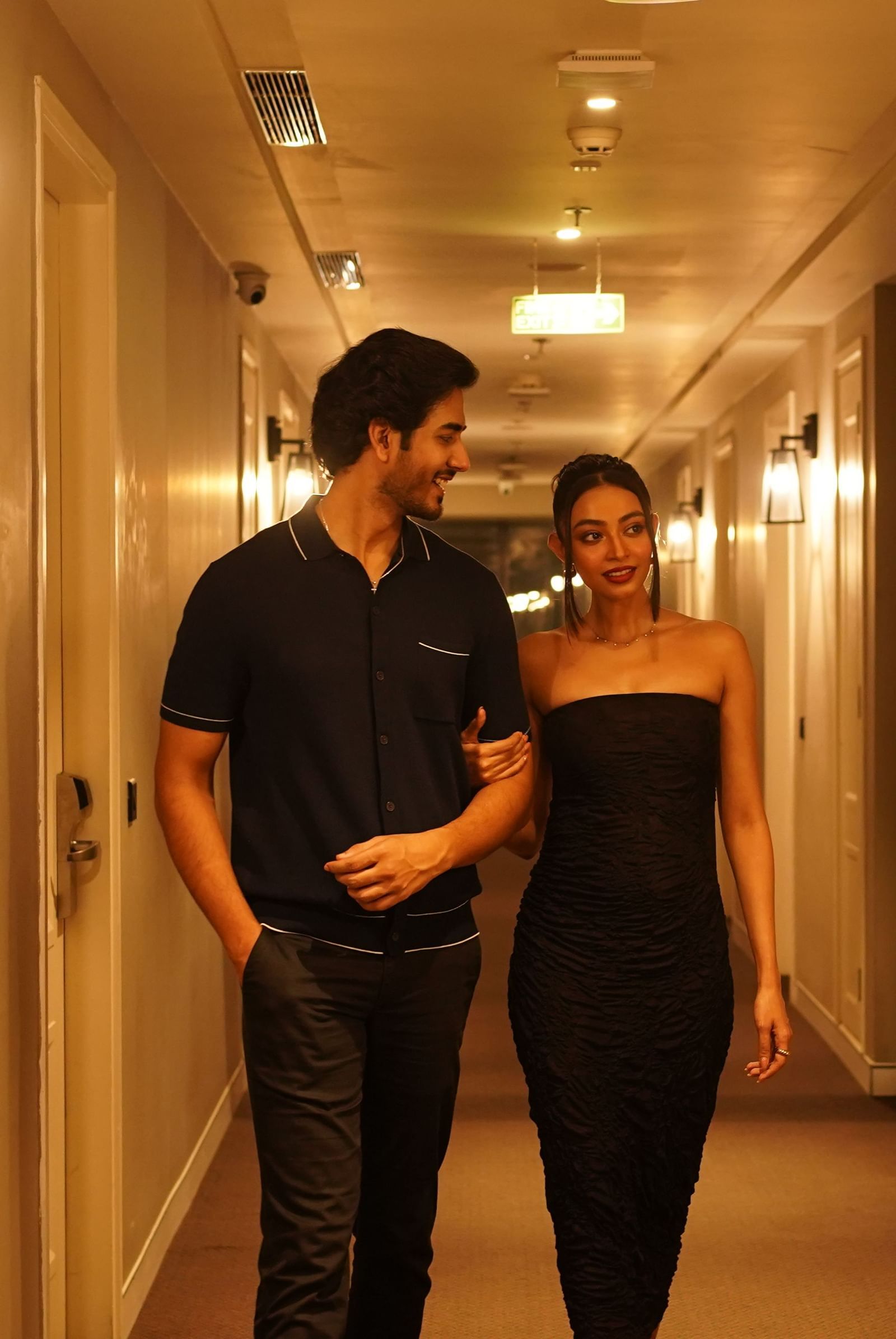 A couple dressed in black walking through the warmly lit corridors to their room - Polo Hotel Agartala