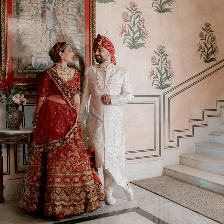 Bride and groom posing by a heritage staircase with floral wall art at Umaid Palace.