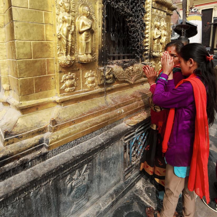Devotees offering prayers at a beautifully carved, golden temple wall.