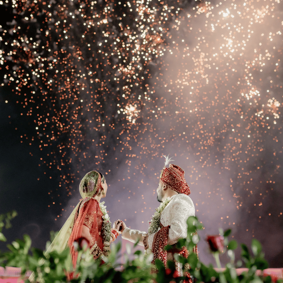 Bride and groom celebrating under fireworks during a night wedding event.