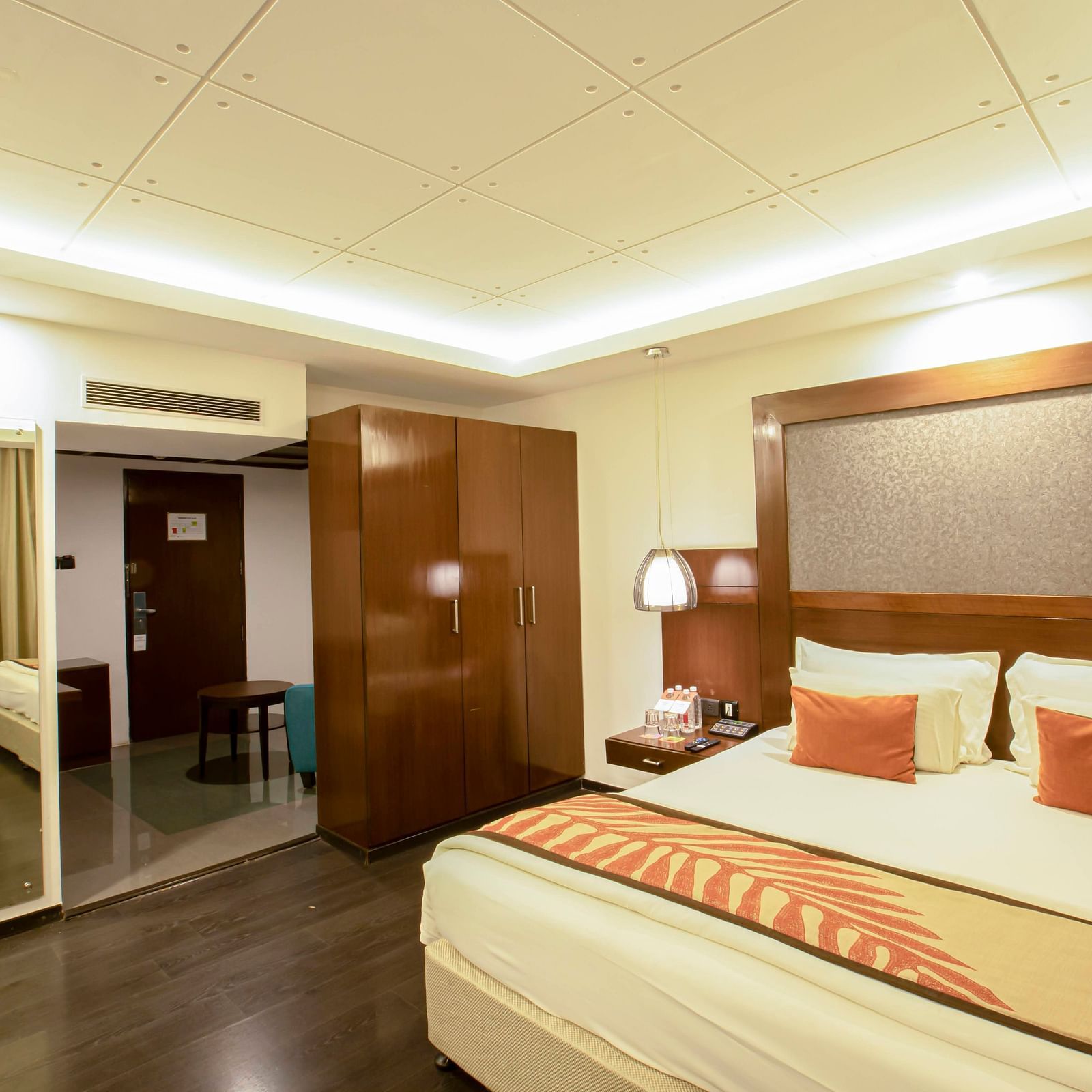 Studio Room at The Cunningham Hotel with warm lighting, a plush bed with a large headboard and a mirror attached to wall next to the wardrobe