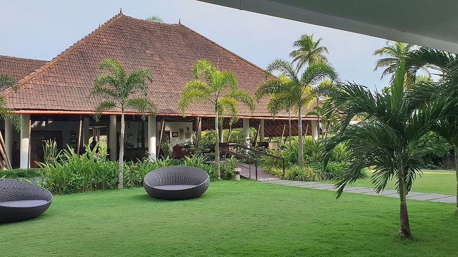 Green lawn interspersed with trees and black lounge chairs - Rhythm Kumarakom