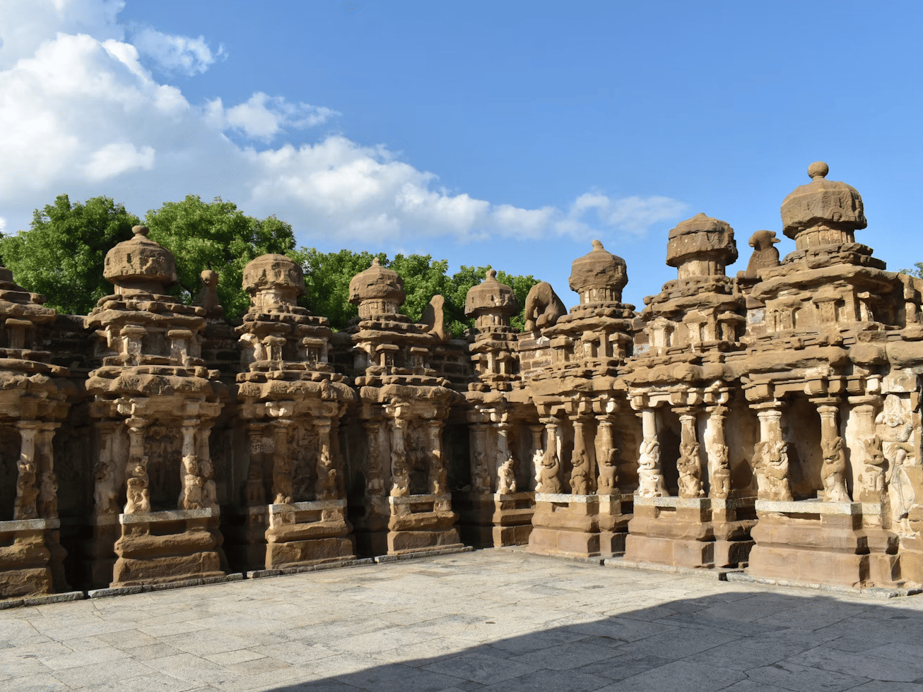 Historic stone temple architecture with multiple small towers and a large courtyard under a sunny sky.