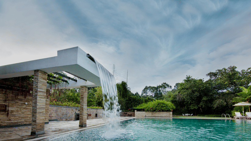 A modern pool with blue water and cloudy skies at Amanvana Spa Resort, Coorg - Luxury Resort
