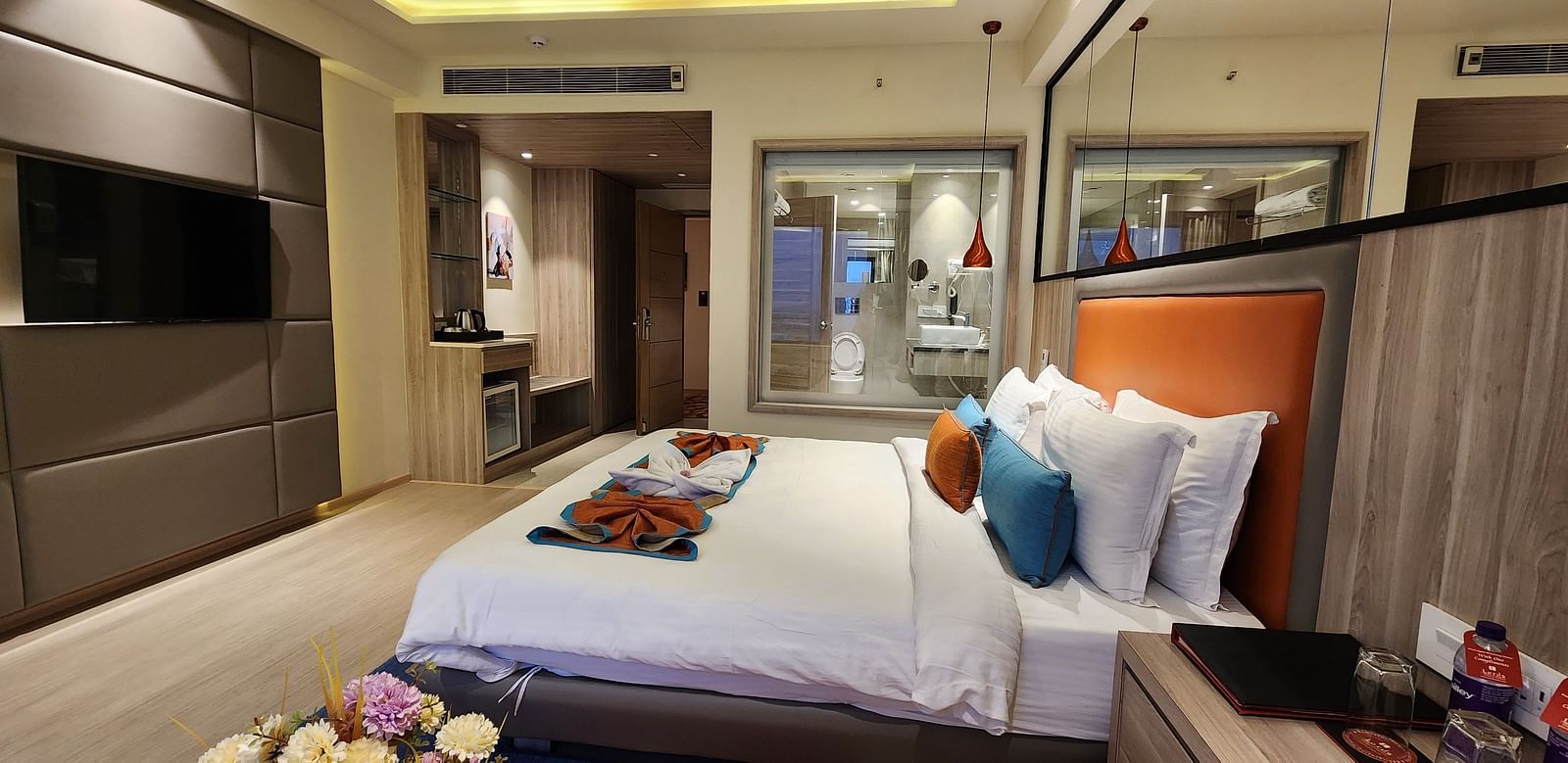 Stylish hotel room with a king-sized bed, colourful cushions, and a glass wall separating the bathroom.