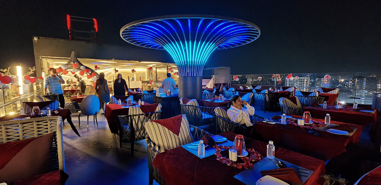 A vibrant restaurant interior with modern blue lighting and red chairs, featuring a central decorative light fixture shaped like a mushroom.
