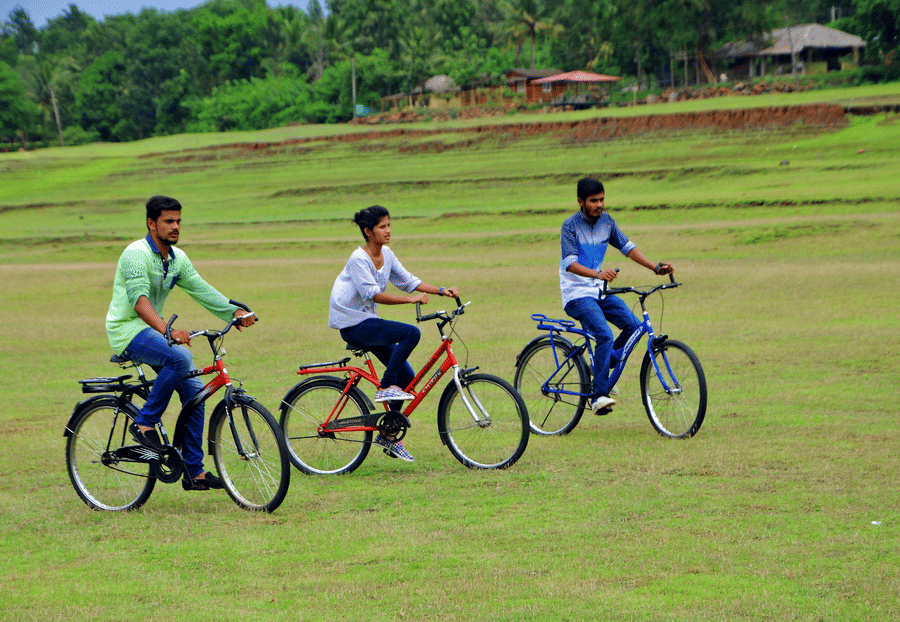 Image of three people cycling in an open area with trees in the background at Coorg Jungle Camp Backwater Resort, Kushalnagar.