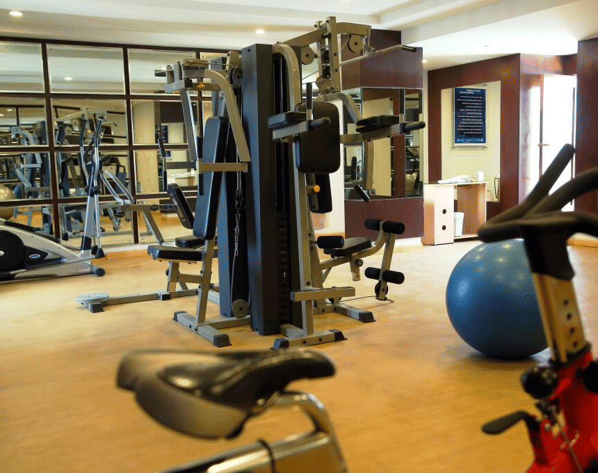 A brightly lit gym featuring cardio machines, a weight machine, and a large blue exercise ball on a wooden floor - Cenneys Gateway