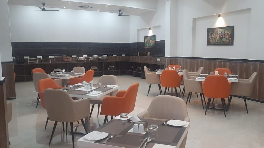 A restaurant shows tables set for dining with dark chairs and lighting - Kankidham Lords Inn