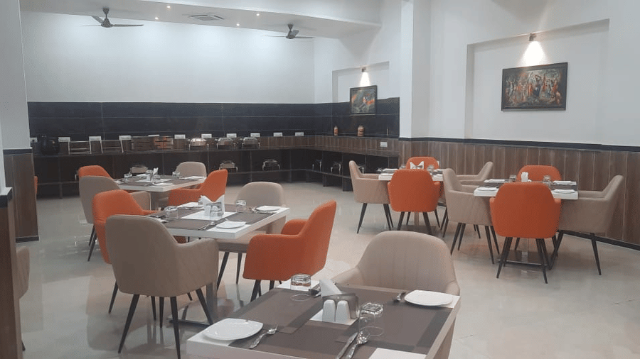 A restaurant shows tables set for dining with dark chairs and lighting - Kankidham Lords Inn