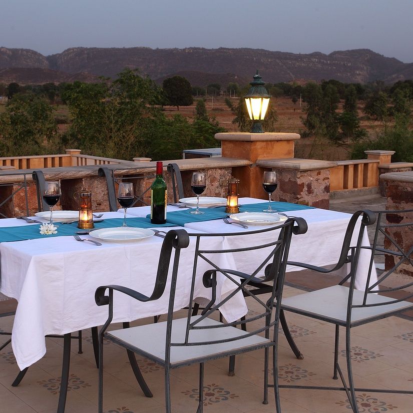 Rooftop dining setup with a white tablecloth, candles, and wine bottle, overlooking scenic hills at sunset at Juna Mahal