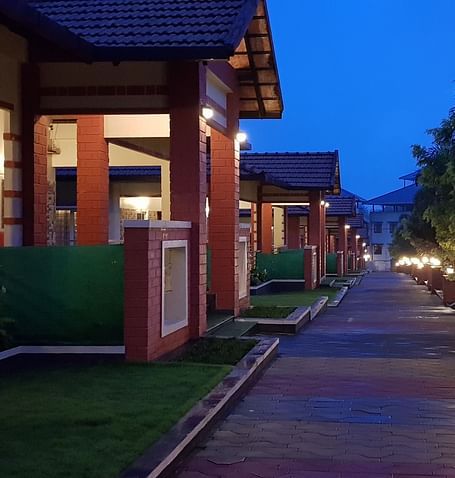 A nighttime view of a building is captured, illuminated by outdoor lighting, with a pathway leading towards it, set against a dark sky | Woodstock Resorts, Coorg