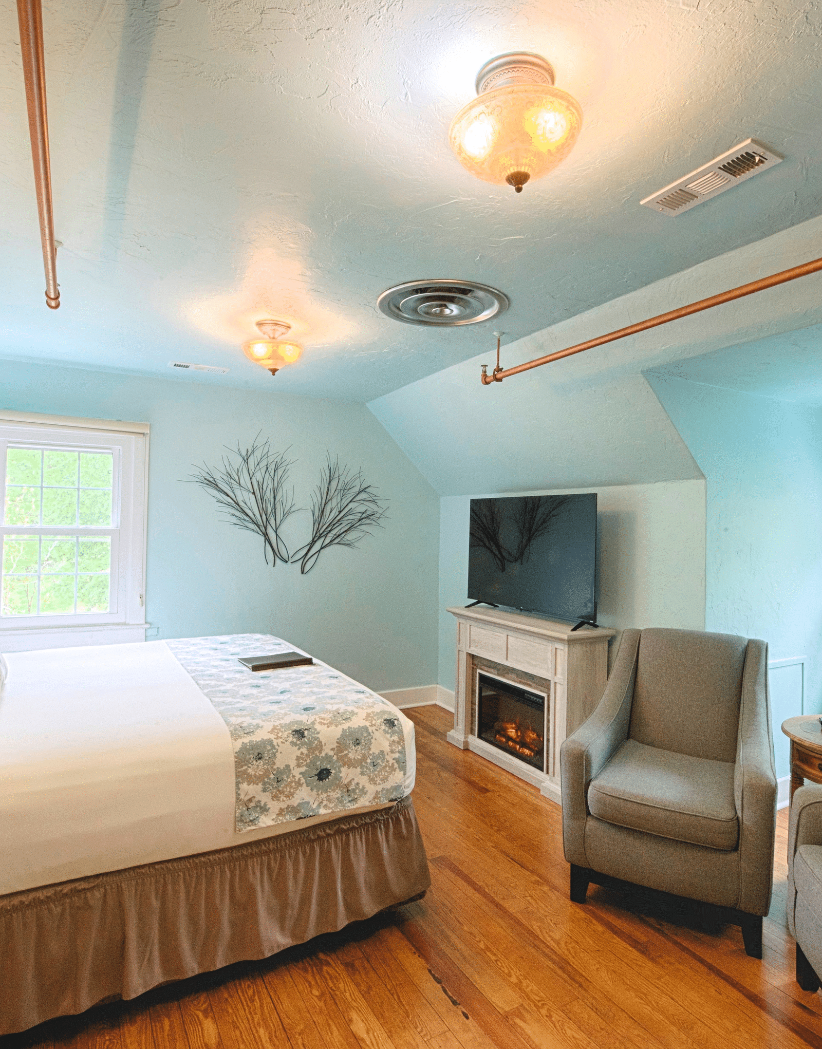 full view image of the laurel suite with pastel blue colored walls along with a flat screen television right opposite to the double bed - Historic Tapoco Lodge