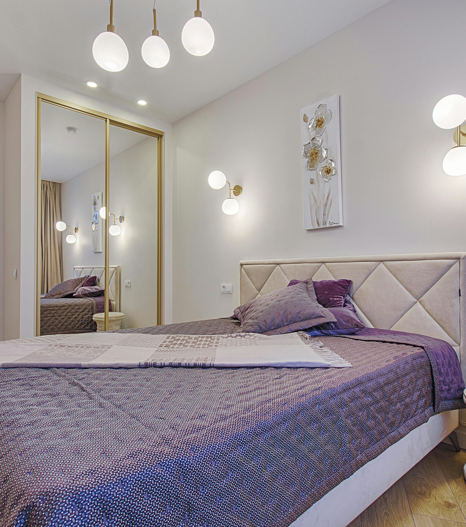 A minimalist bedroom with a quilted purple bedspread, a diamond tufted headboard, and mirrored wardrobe doors.
