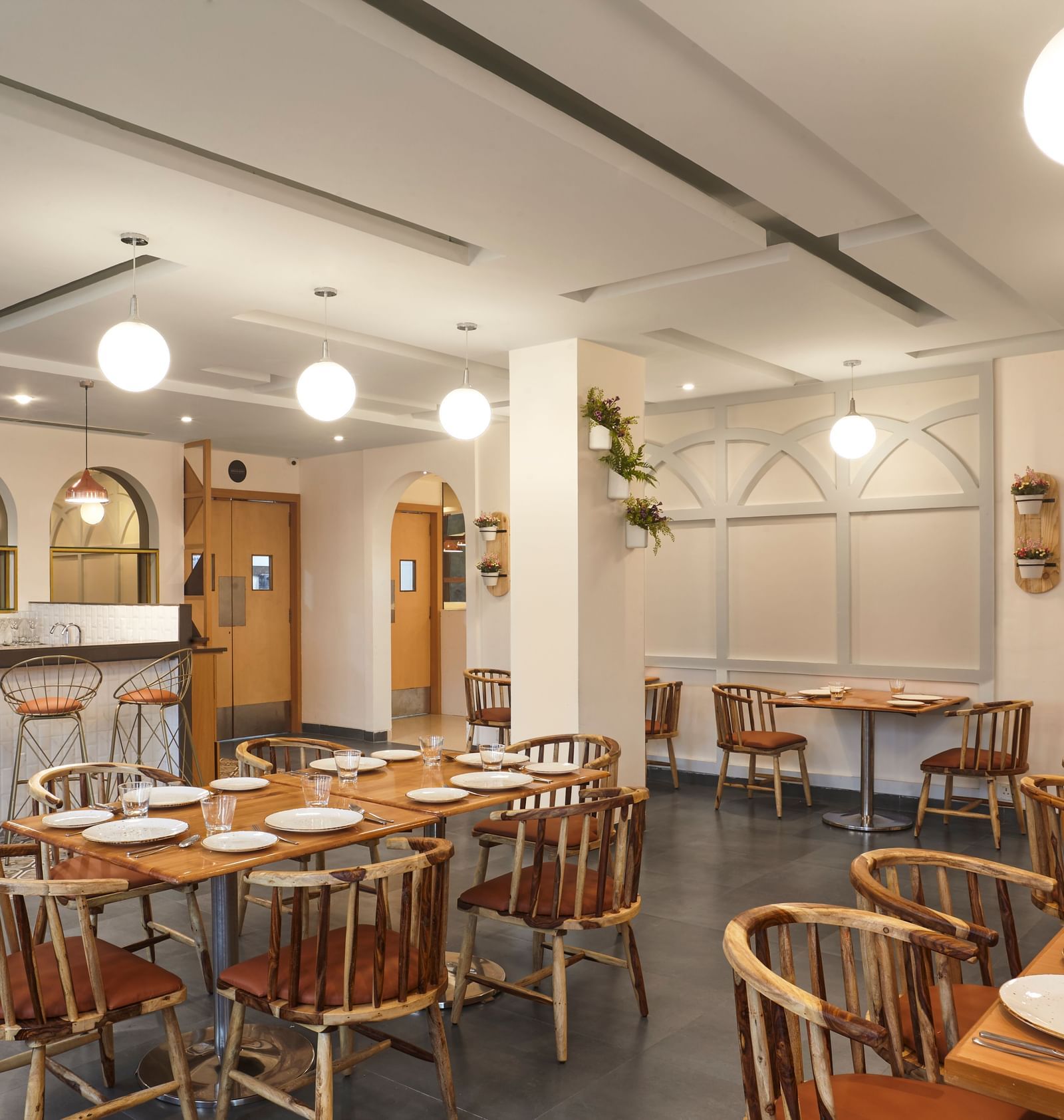 The spacious dining hall at Monday Hotels Mahape, Navi Mumbai, with multiple wooden tables and a central bar.