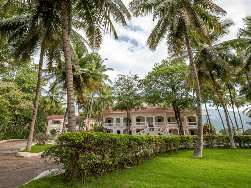 A grand colonial-style exterior of Black Thunder Resort with arched balconies, nestled amongst lush palm trees and manicured green lawns.